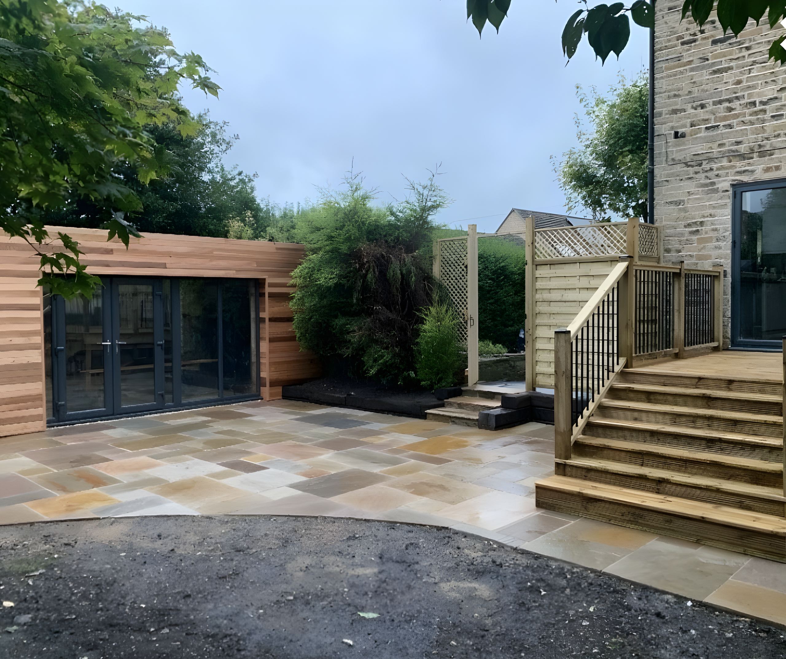 Raised timber deck with balustrade and steps down to an Indian stone patio, beside a cedar clad garden room